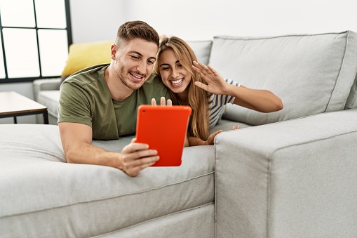 Young hispanic couple using touchpad lying on the sofa at home.