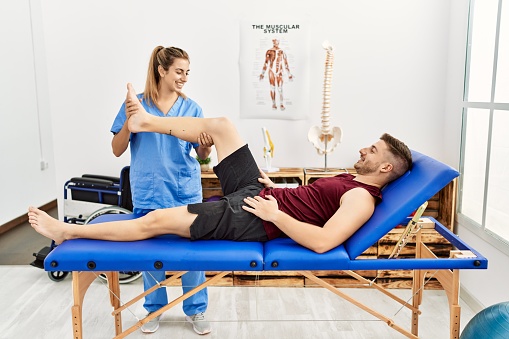 Young hispanic physioterapist woman make legs rehab treatment to man at the clinic.