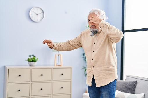 Middle age grey-haired man suffering dizzy standing at home