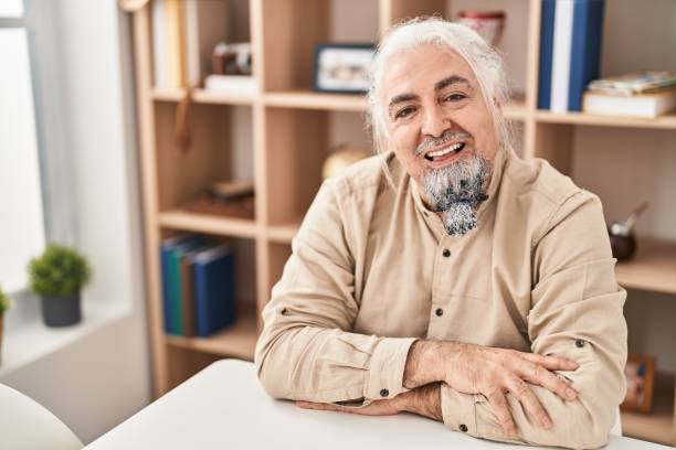 istock Middle age grey-haired man smiling confident sitting on table at home 1437902597
