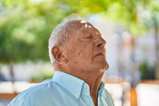 Senior grey-haired man breathing at park