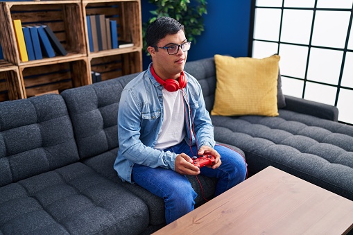 Down syndrome man playing video game sitting on sofa at home