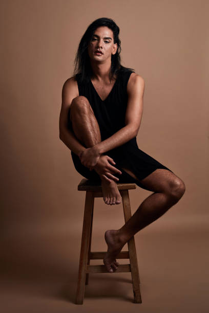 Fashion, beauty and inclusion with a gender neutral man or model posing in studio on a chair or stool against a brown background. Lgbt, equality and empowerment with a contemporary, stylish male Fashion, beauty and inclusion with a gender neutral man or model posing in studio on a chair or stool against a brown background. Lgbt, equality and empowerment with a male sitting alone inside gender neutral photos stock pictures, royalty-free photos & images