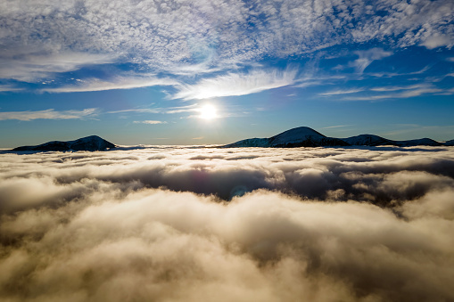 Aerial view of vibrant sunrise over white dense clouds with distant dark mountains on horizon.