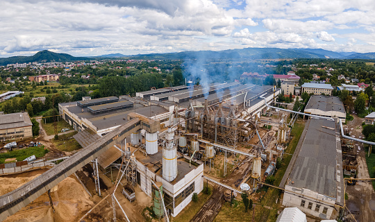 Aerial view of wood processing plant with smokestack from production process polluting environment at factory manufacturing yard.