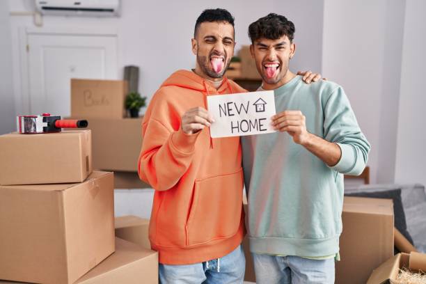 Young hispanic gay couple moving to a new home sticking tongue out happy with funny expression. stock photo