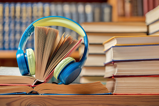 A DSLR photo of headphones with stacks of books at the library. Can illustrate the concept of audio books. Shallow depth of field.