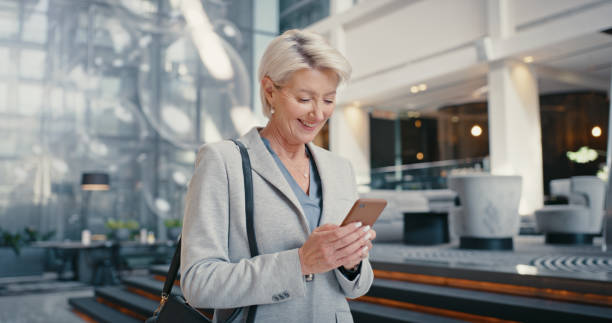 teléfono, mujer corporativa feliz y sonrisa leyendo noticias en línea o videoconferencia en el lugar de trabajo moderno. empresaria senior, notificación por correo electrónico y aplicación de internet de comunicación de mensajes móviles de tecnolog� - airport newspaper travel business travel fotografías e imágenes de stock