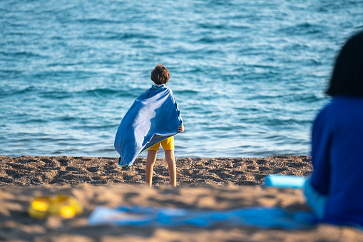 Rare photo of mother and son sitting on a blue mat on the beach. Mother is wearing a blue dress while 9 years old boy is seen covered with a blue beach towel. Shot under daylight with a full frame mirrorless camera.