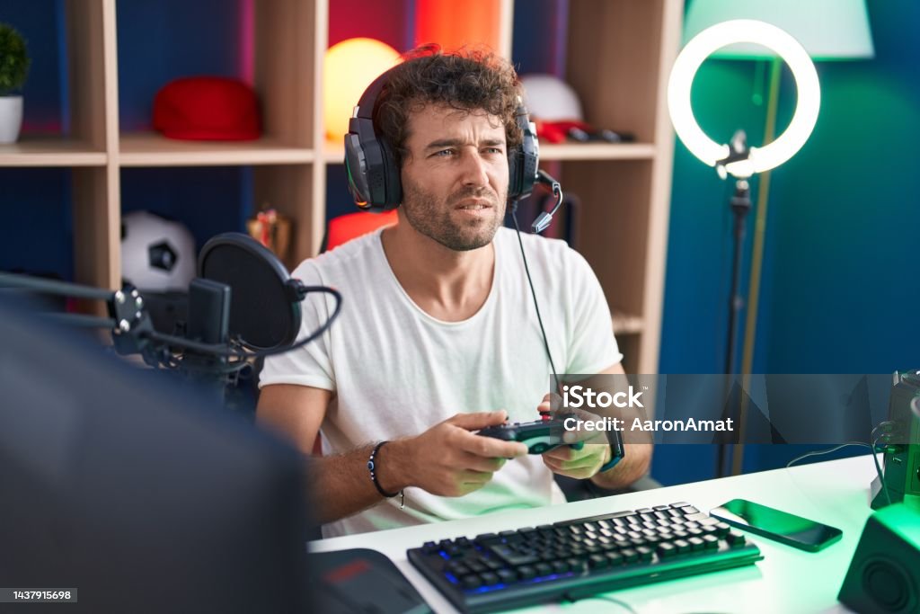 Young hispanic man streamer playing video game using joystick at music studio Adult Stock Photo