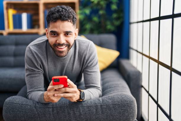 istock Young hispanic man using smartphone lying on sofa at home 1437917604