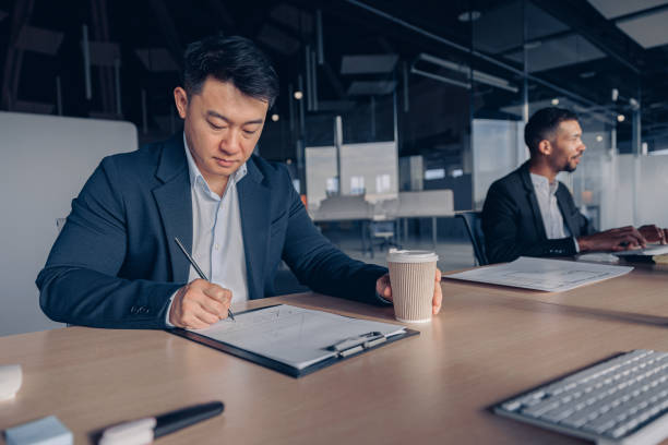 istock Focused asian businessman drinking coffee while working with documents in modern office 1437920892
