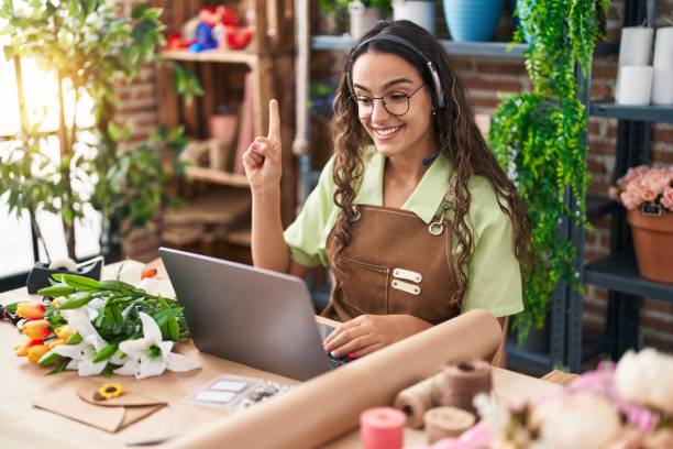 jeune femme hispanique travaillant chez un fleuriste faisant un appel vidéo souriant avec une idée ou une question pointant du doigt avec un visage heureux, numéro un - gardening humor meeting conference call photos et images de collection