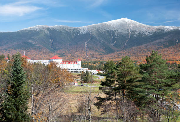 Colorful autumn scene at Bretton Woods, New Hampshire. Blue sky with dusting of snow on summit of Mount Washington, vibrant fall foliage, and red roof of historic Mount Washington Grand Hotel.