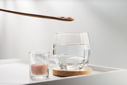 Add pink himalayan mineral salt to your drinking water for health on a white table