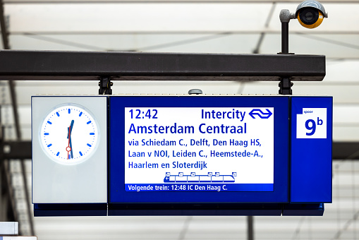 23.10.2022 Amsterdam Centraal Train Station, Netherlands. Train time display screen at central railway station in Amsterdam city centre. Blue sign with clock display sowing time of next train platform