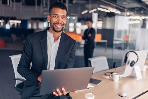 Portrait of african businessman with laptop looking in camera and smiling Portrait of african businessman with laptop looking in camera and smiling on colleague background black man laptop stock pictures, royalty-free photos & images