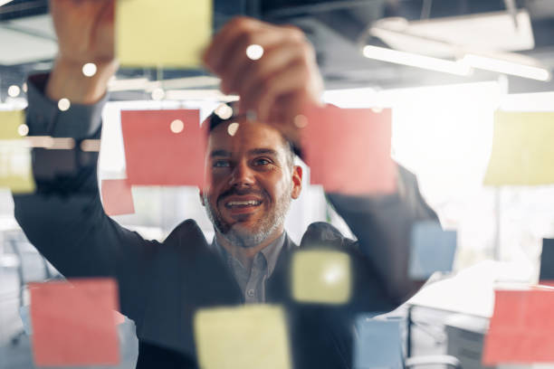 Close up of smiling businessman is glues sticky notes on motivation board in modern office stock photo