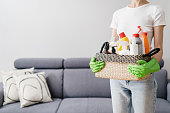 woman in gloves hold basket with cleaning supplies indoors