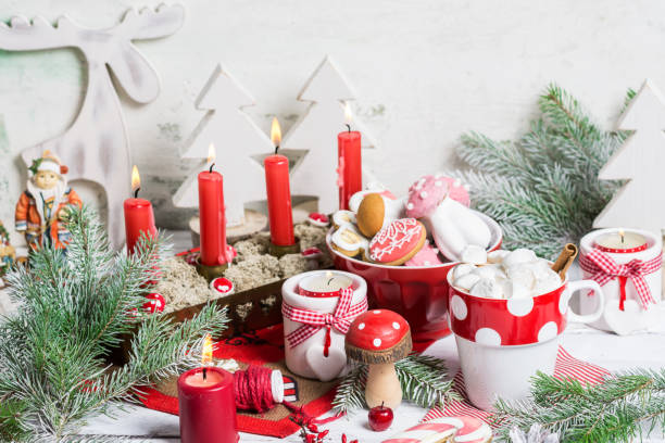 istock Christmas composition with marshmallows in white red cup with cocoa and cinnamon stick on white wooden table decorated with burning candles, gingerbread cookies mushrooms, fir tree branches 1437925325