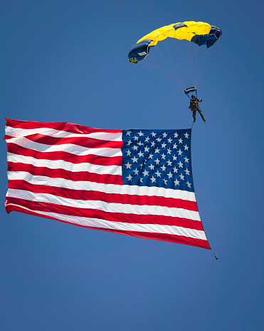 A low angle shot of a man in the parachute with USA flag in a clear blue sky