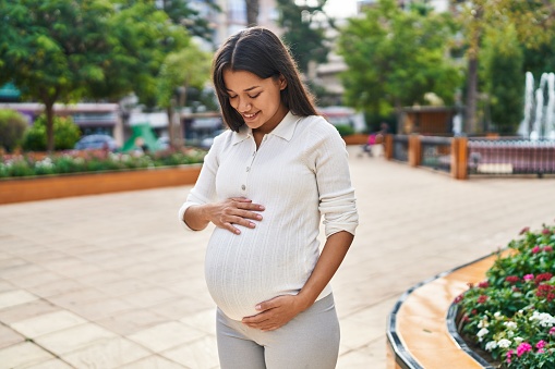 Young latin woman pregnant smiling confident touching belly at park