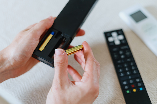cropped shot of female hands insert new battery in tv remote control for watching television at home