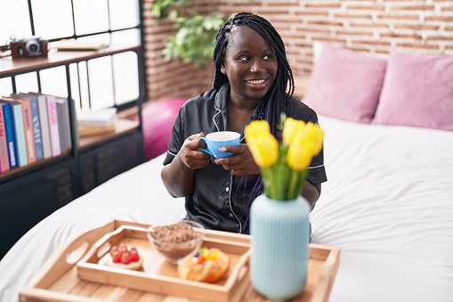 African american woman having gift breakfast sitting on bed at bedroom