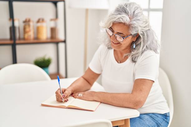 istock Middle age woman writing on notebook sitting on table at home 1437926495