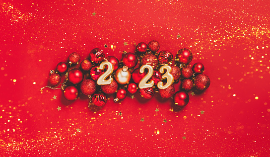 New year 2023 celebration. Date 2023 on a red background of Christmas toys, balls, serpentine, sparkles. Beautiful festive New Year's mockup on a dark background. new year christmas concept