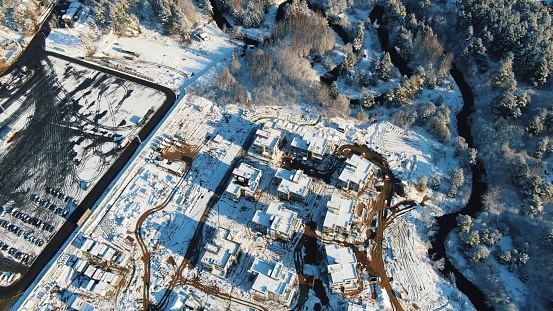 Sports and recreation concept. Aerial view of the winter cottages construction on the modern ski resort surrounded by forest.