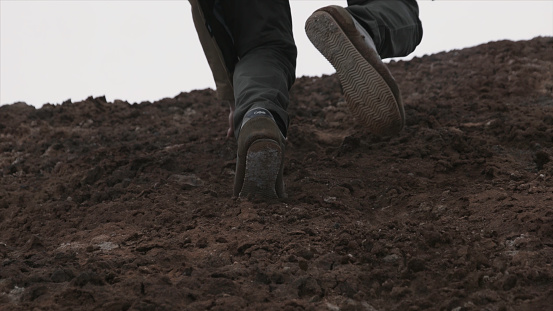 Close up of hiking boots and legs climbing up rocky trail. Close up climber legs make a last steps before peak. Close up of man foot in the moutain.