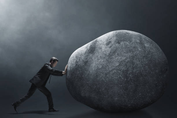 istock Business man pushing big stone on dark background 1437928527