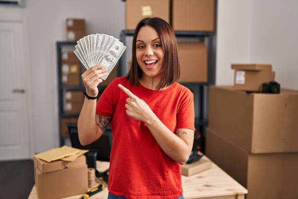 mulher hispânica jovem que trabalha no comércio eletrônico de pequenas empresas segurando notas sorrindo feliz apontando com a mão e o dedo - bill looking cheerful latin american and hispanic ethnicity - fotografias e filmes do acervo