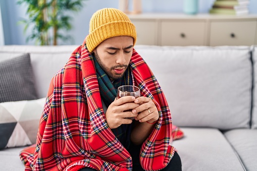 African american man covering with blanket drinking water at home