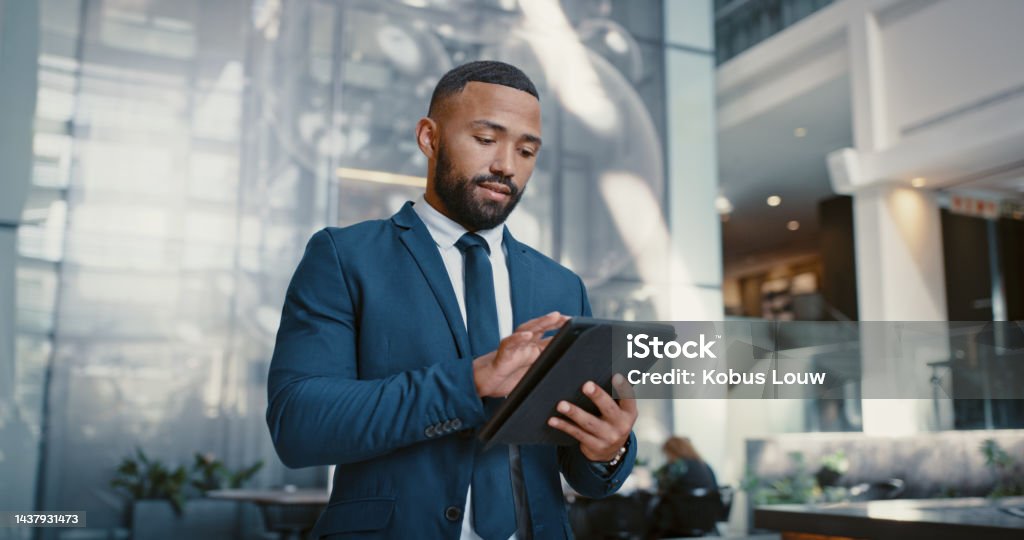Hotel, manager and man on a digital tablet for booking, planning and accommodation management while working at front desk. Black man, concierge and hospitality by male doing online task at reception Manager Stock Photo