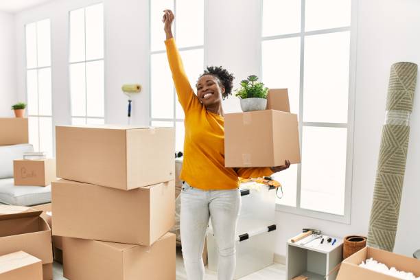 African american woman holding package standing with winner expression at new home stock photo