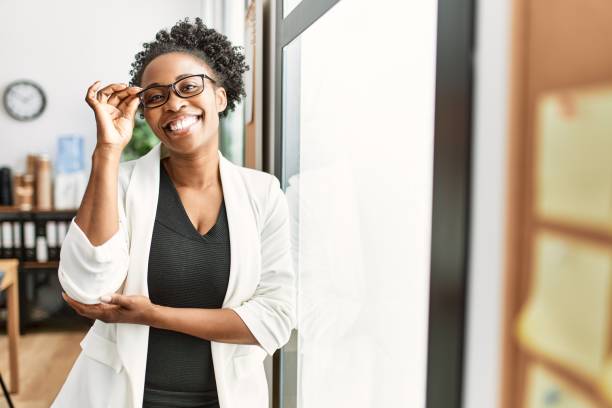 アフリカ系アメリカ人の女性ビジネスワーカーが自信を持ってオフィスに立って微笑む - beautiful indoors looking at camera cheerful ストックフォトと画像