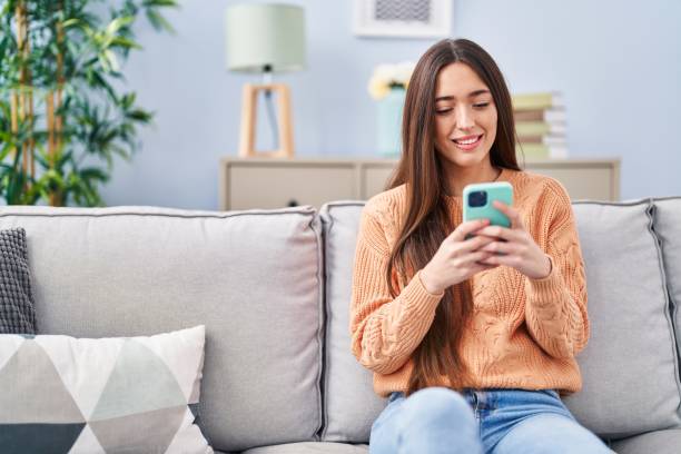istock Young beautiful hispanic woman using smartphone sitting on sofa at home 1437932480