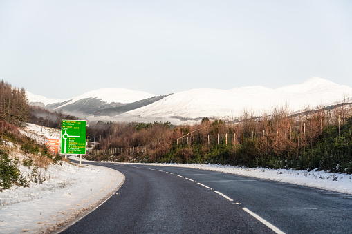 A driver perspective on a journey in the Trossachs, Scotland, approaching  a sign giving direction information for an approaching roundabout.