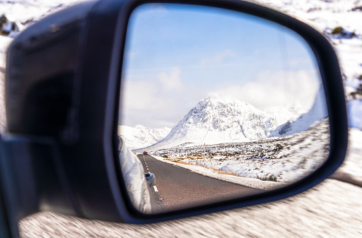 A driver's view of a car's wing mirror on a journey through Glencoe, in Scotland's Highlands, during snowy winter weather.