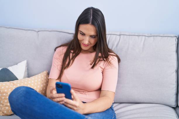 istock Young beautiful hispanic woman using smartphone sitting on sofa at home 1437934745