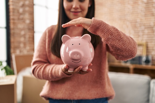 Young hispanic woman smiling confident holding piggy bank at new home