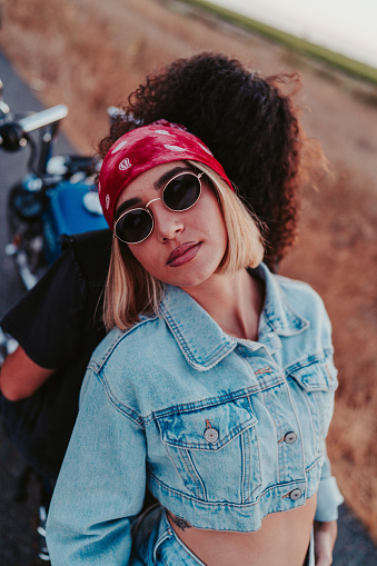 A high angle shot of a confident blonde female wearing a denim outfit and posing on a motorcycle with her partner