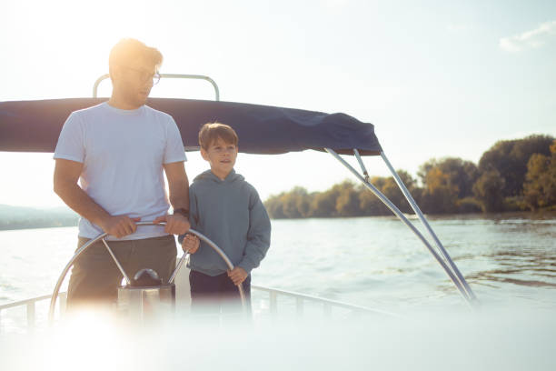 Father and son together steer a ship sailing on a river stock photo
