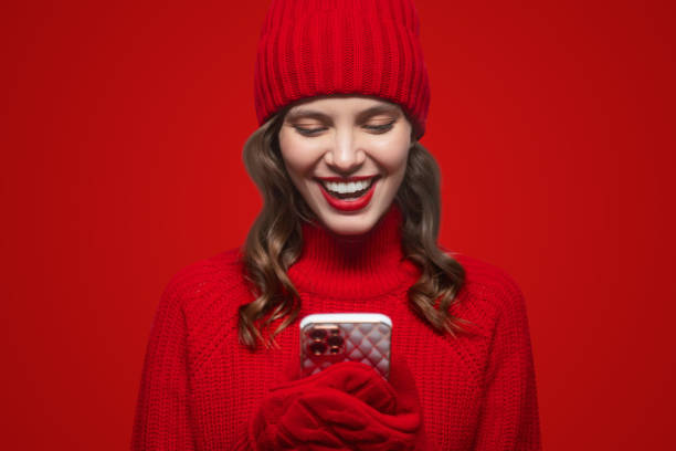 istock Pretty woman in knitted mittens using video chat on phone on red background 1437941247