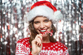 Portrait of woman with christmas candy wearing santa hat isolated on tinsel background