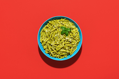 Trofie al Pesto, a delicious Italian dish minimalist on a red-colored table. Short pasta called Trofie with pesto sauce and parmesan.