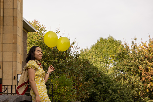 Young Asian woman having fun with yellow balloons outdoor