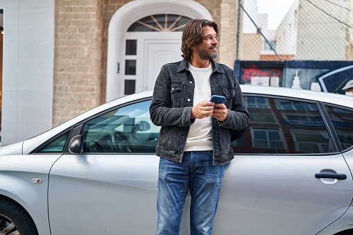 Middle age man using smartphone leaning on car at street